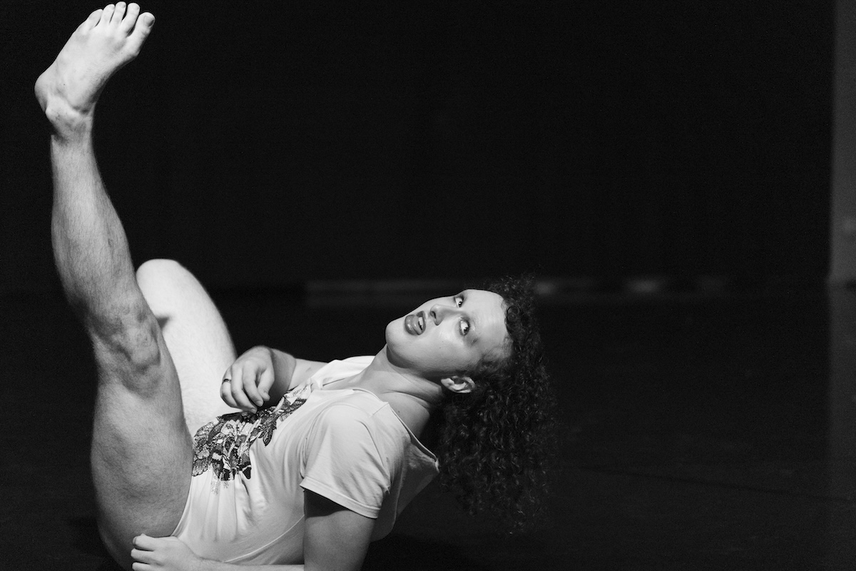 Black and white photo of dancer Alix Kuijpers performing on stage, lying on his back with one leg extended upward in a expressive pose.